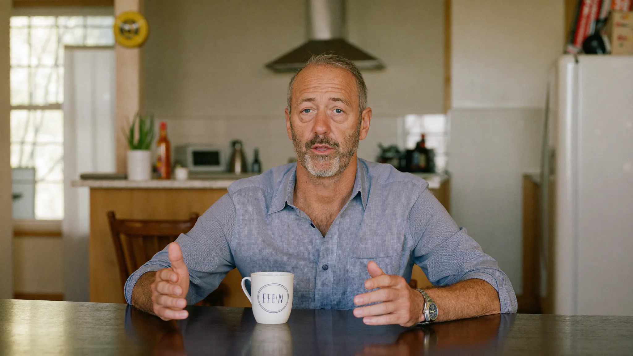 A man in his late forties at his kitchen table, speaking straight to camera